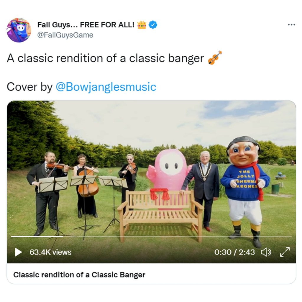 A tweet from @FallGuysGame saying "A classic rendition of a classic banger. Cover by @Bowjanglesmusic" above a video of a string trio, an inflatable bean from Fall Guys, the mayor of Skegness and the town mascot standing beside the Fall Guys bench. The mayor looks very confused.