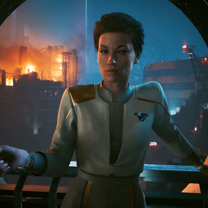 A woman from the Cyberpunk 2077: Phantom Liberty teaser trailer. She has short hair and is wearing a suit with a New United States of America pin in the breast pocket.