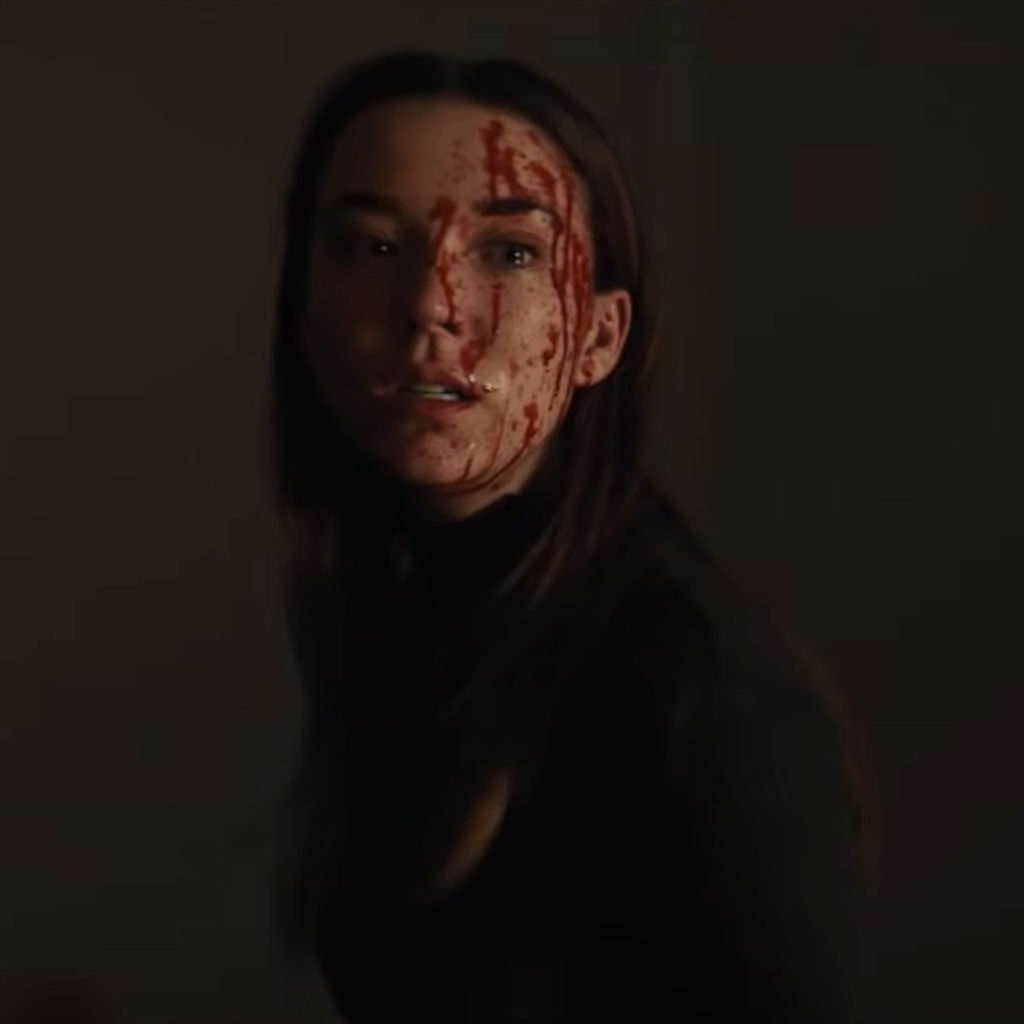 Nicole Brydon Bloom as Sarah, with a blood spatter on her face, in the horror movie Apartment 1BR.
