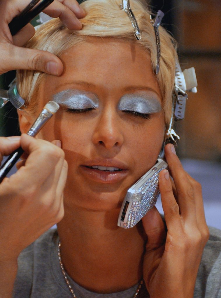 Best blue eye makeup: Paris Hilton sits on phone while shimmery eyeshadow is applied on her in 2003