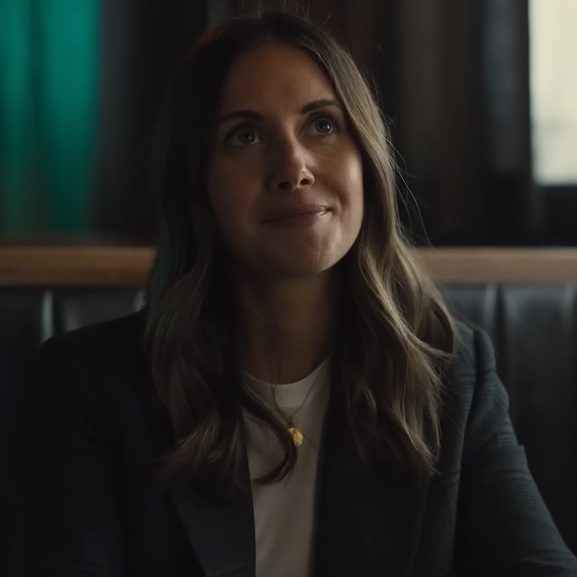 Alison Brie as Ally in Somebody I Used to Know. She's sitting in a bar booth with a subtle smile.