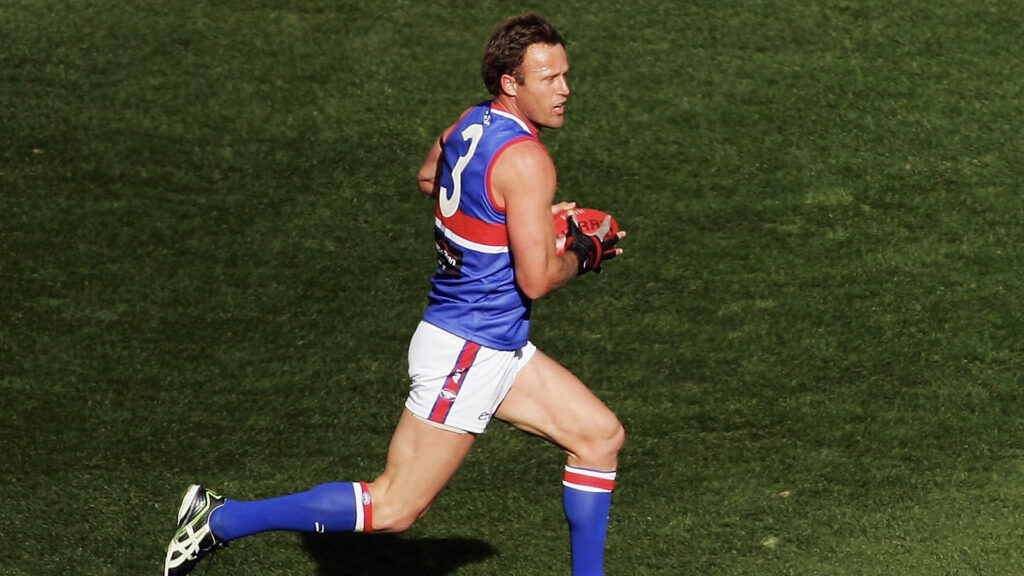 Chris Grant, AFL player, running on field holding football.